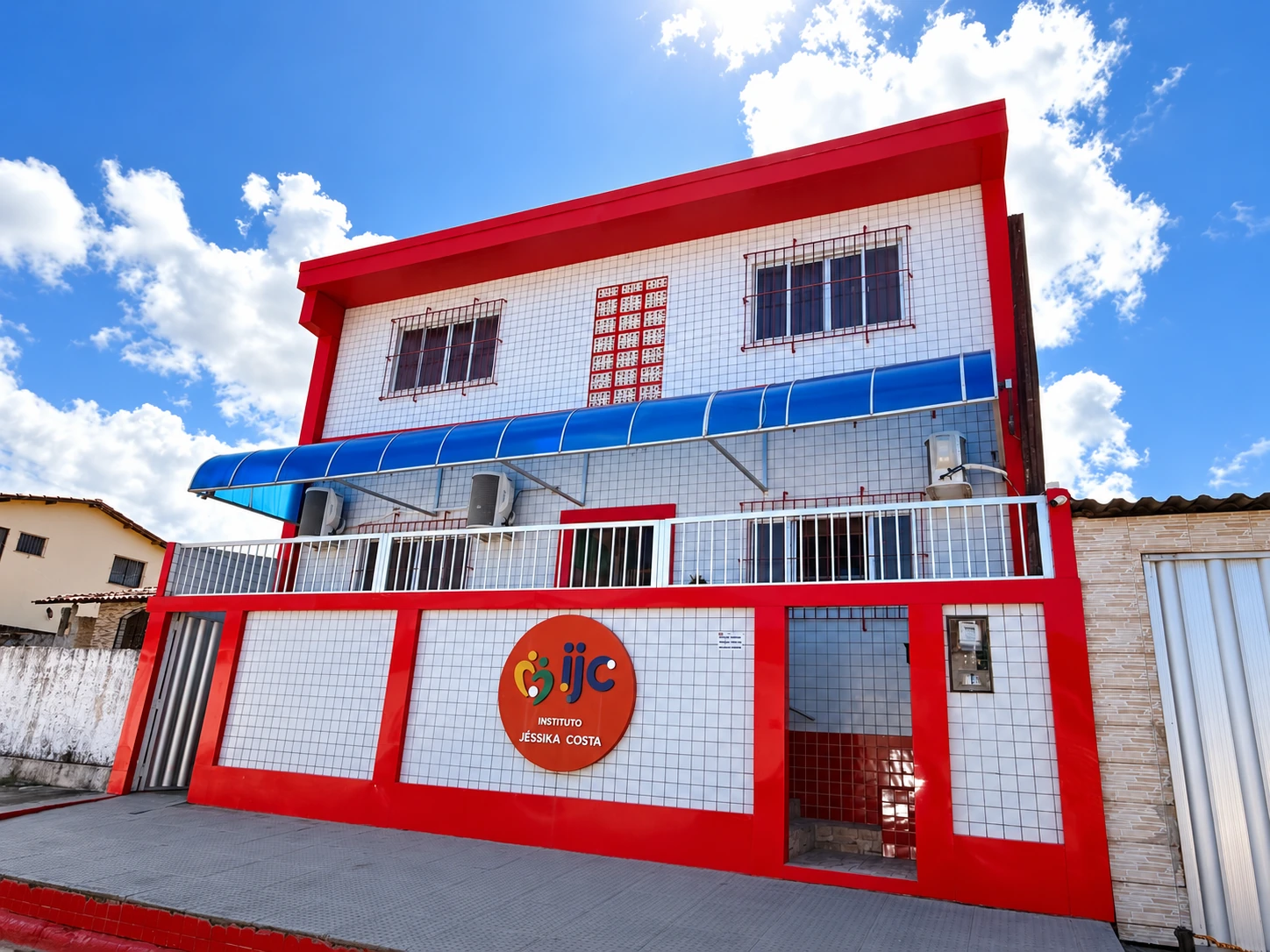 Fachada do Instituto Jéssika Costa, com revestimento branco, estrutura vermelha e toldo azul.